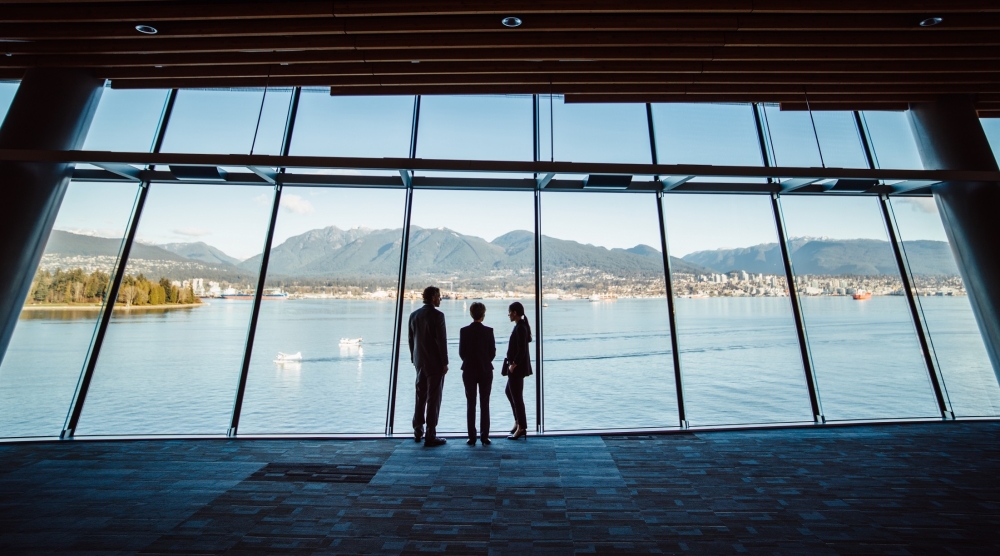 Three people looking out the window over the water in a convention centre in Canada
