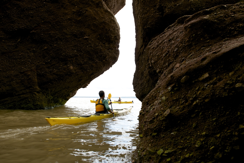 Person in a yellow kayak on the water in between two large rocks during the day image